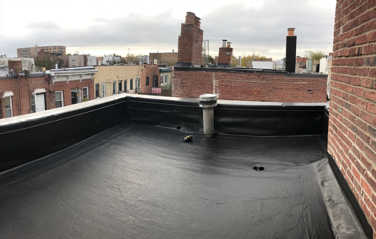 Black EPDM rubber membrane on a Brooklyn row house flat roof, seams and drain freshly detailed
