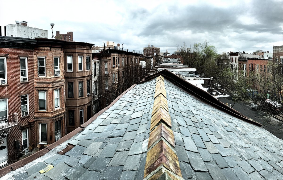 Grey natural slate roof on a Brooklyn brownstone, rows of slate laid in even courses below the cornice